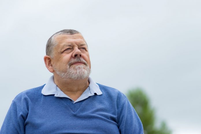 Outdoor portrait of a bearded senior man looking up with hope