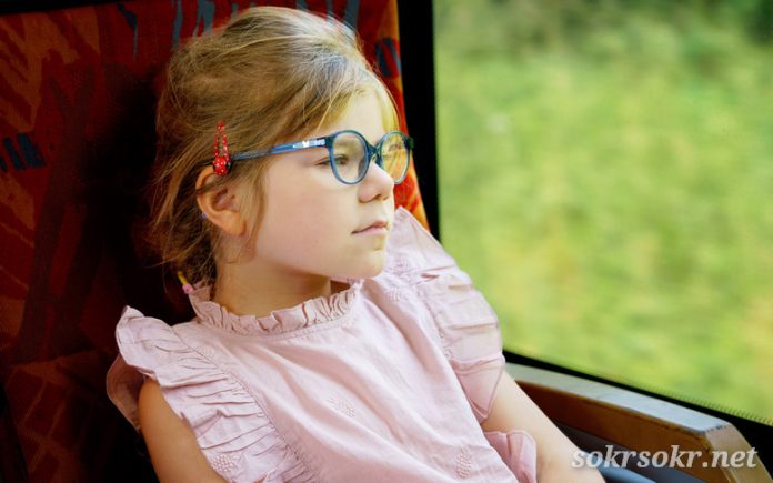 Little presНе оставлю тебя, не забудуachool girl with glasses sitting in train and looking out of window while moving. Happy child , smiling child going on family vacations by railroad or making weekend trip.
