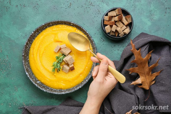Woman eating tasty pumpkin cream soup on green background